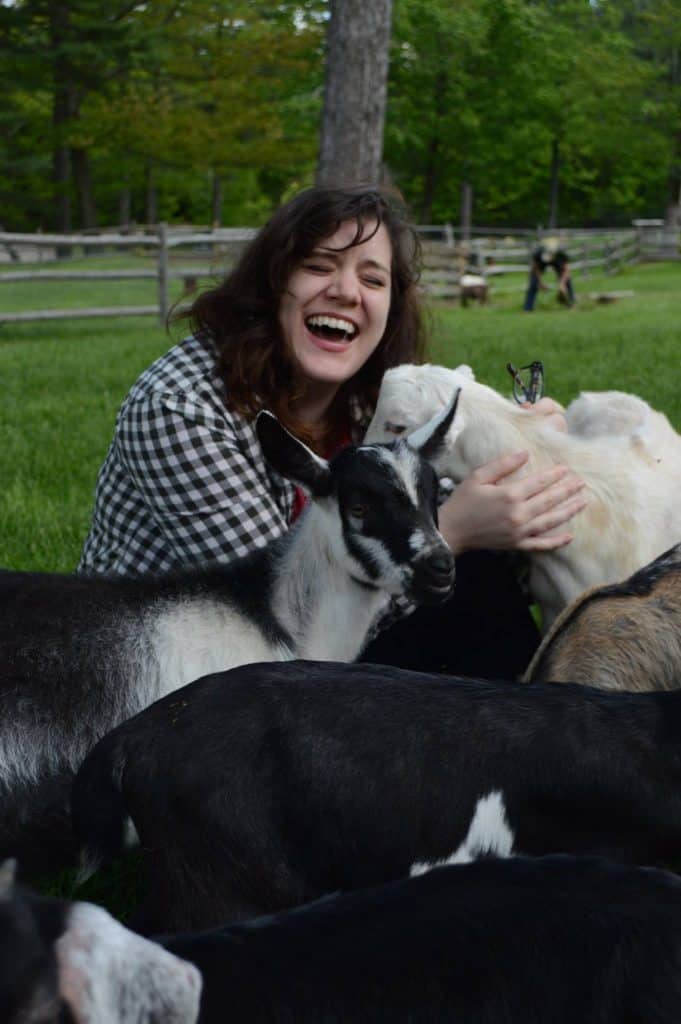 Girl smiling in a black and white plaid shirt hugging a goat.
