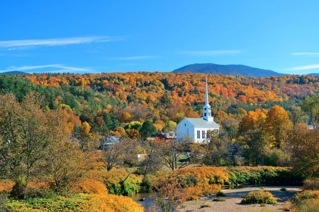 Aerial view of the mountains with fall leaves and a white church with steeple in the midst of them at a New England vacation destination