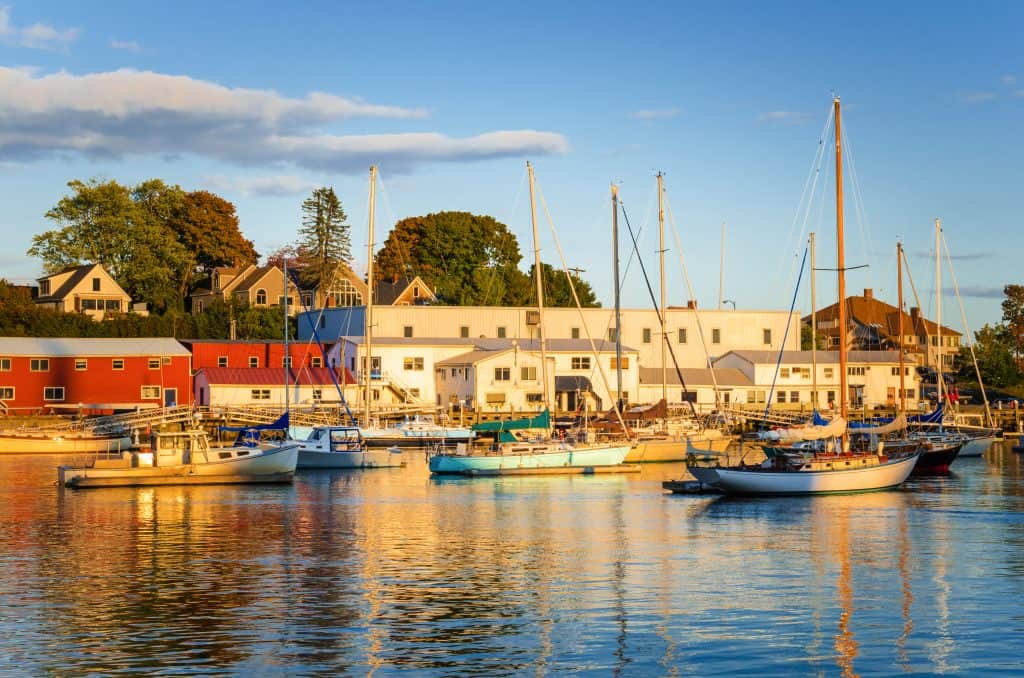 Many boats in a harbor with buildings in the background in a popular New England getaway spot