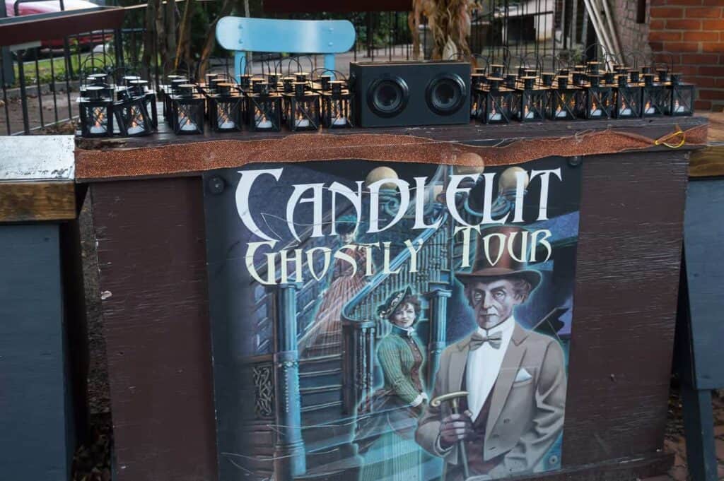 Sign reading "Candlelit Ghostly Tour attached to a table with dozens of lanterns on top