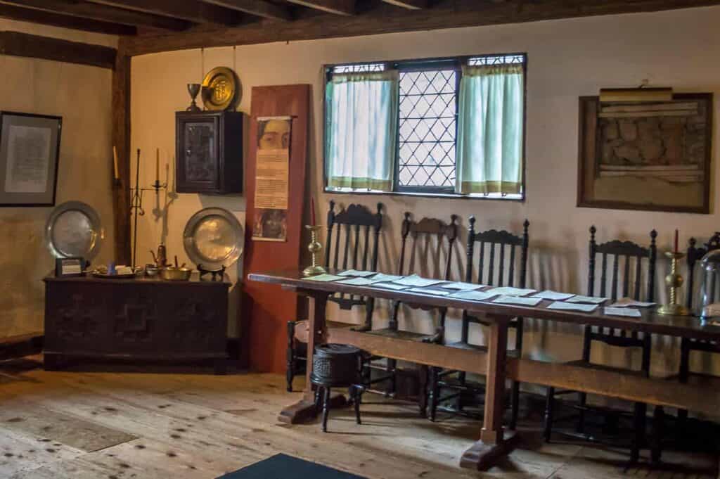 A historic room filled with period furniture; table and chairs lined up in front of the window