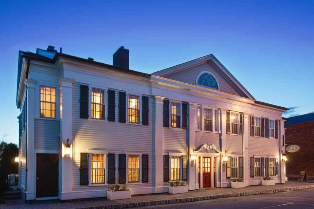 Large white hotel with black shutters and a red door under a dark blue sky.