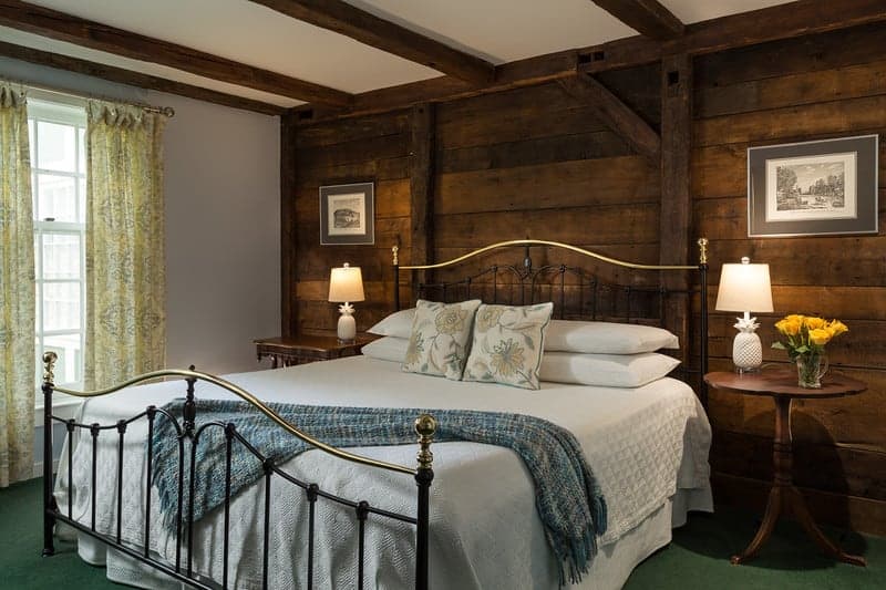 A big bed with a brass headboard and footboard and a white bedspread in a romantic New England hotel room