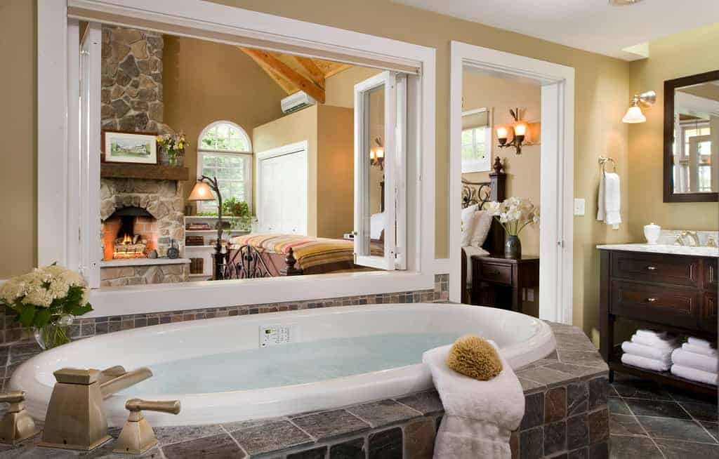 A large bathtub next to a window opening into the next room