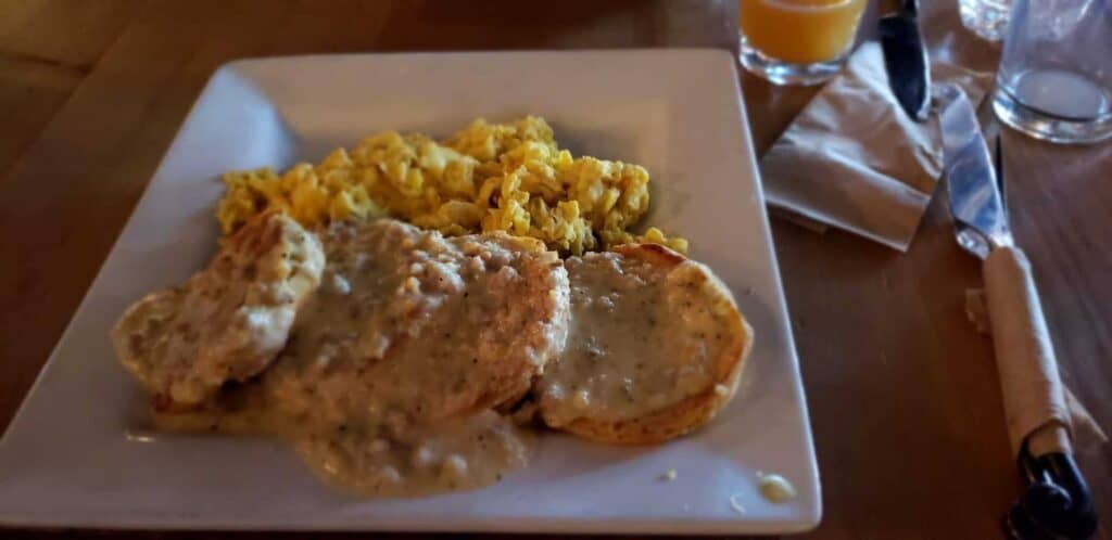White plate with eggs as well as biscuits covered in gravy.