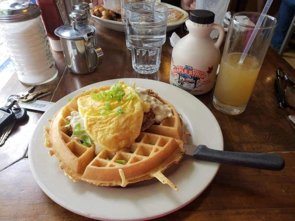 Waffle on a white plate, stacked high with eggs and green onion.