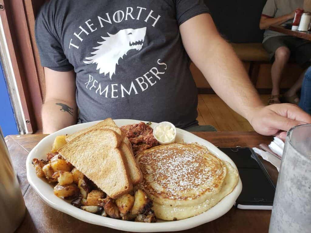 Breakfast on a plate featuring toast, potatoes, and a pancake.