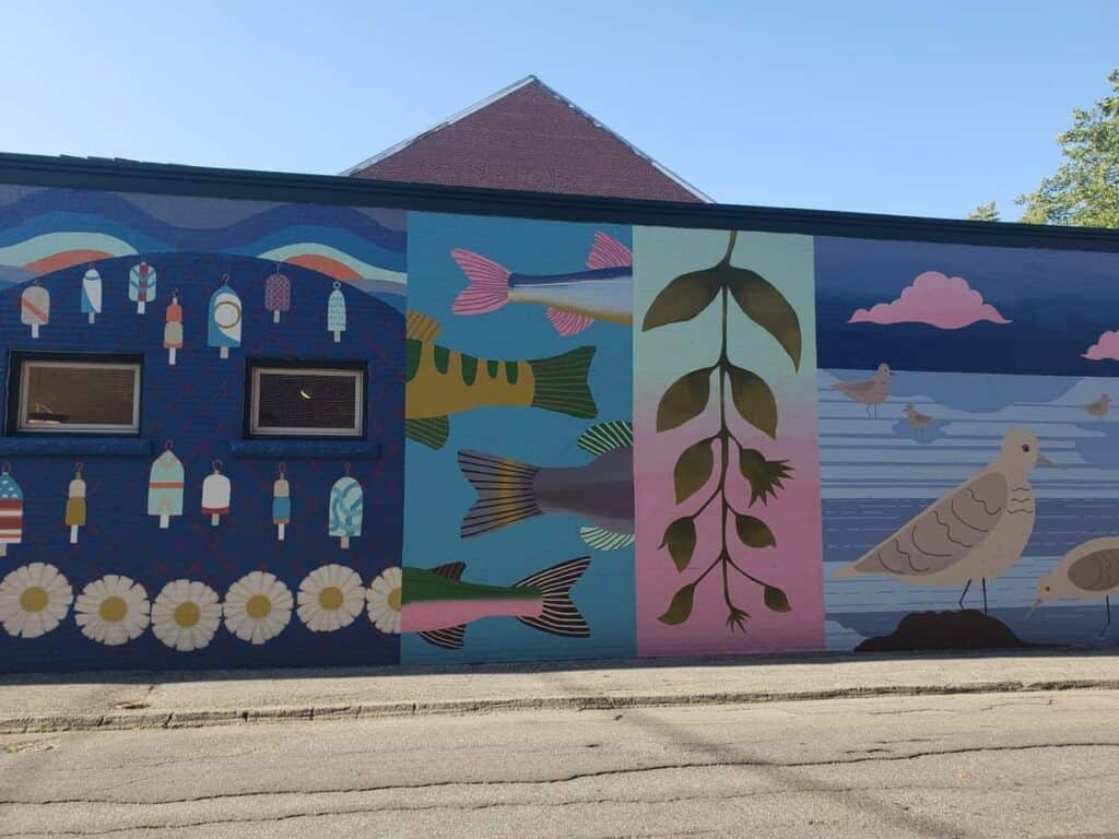Street art on the side of a building, featuring fish, birds, and leaves on an empty street.