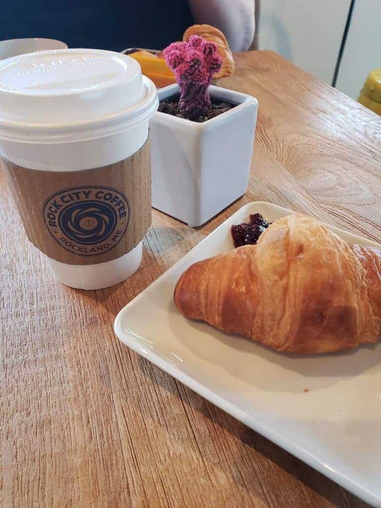 A plate of a croissant and a cup of coffee on a table.