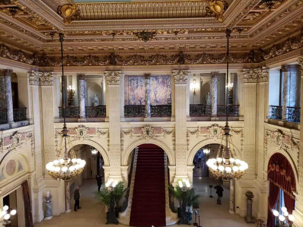 Looking down toward a red staircase and two chandeliers in a ballroom