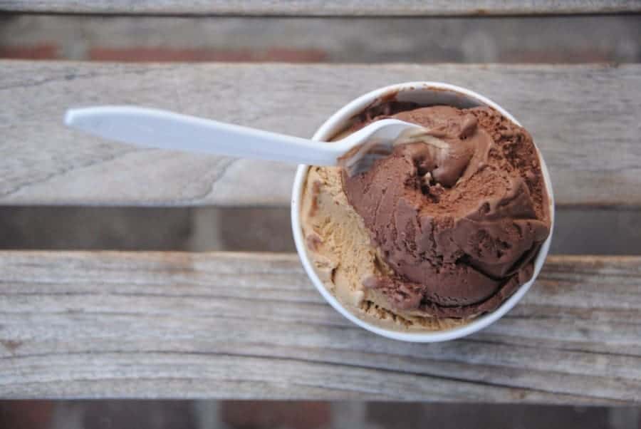 Spoon sitting in a pint of chocolate ice cream on a picnic table.