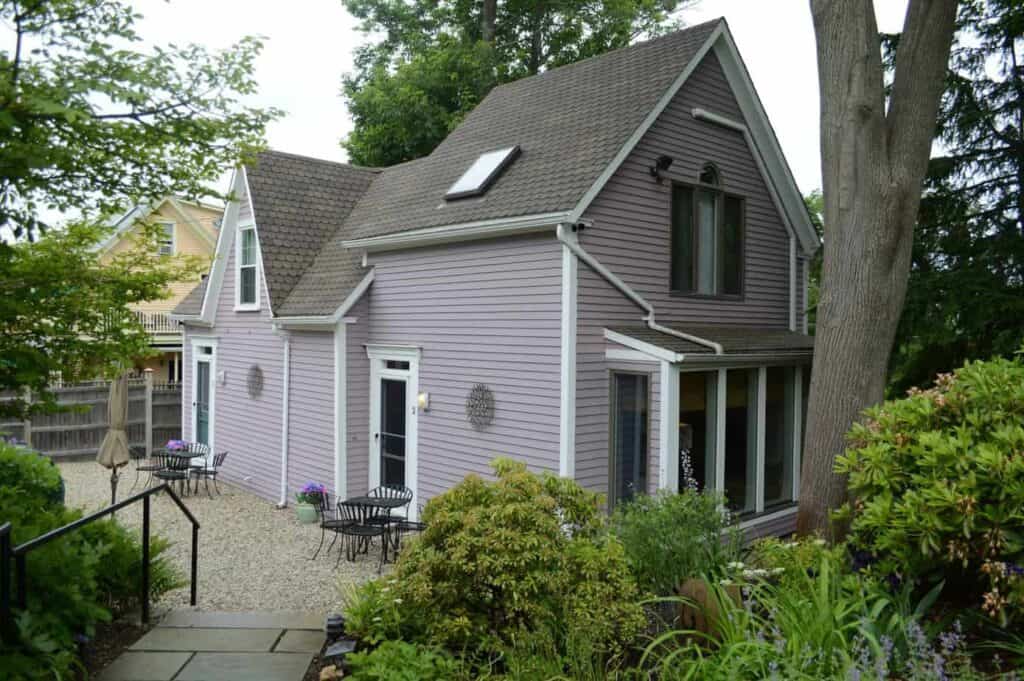 A purple building with black window shutters sits surrounded by greenery.