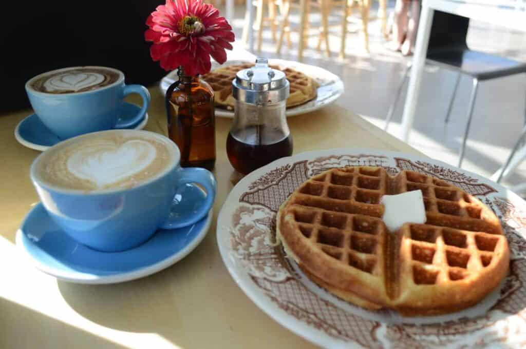 A plate of food on a table, featuring coffee in a blue mug and a waffle with butter on it at a Burlington VT coffee shop.