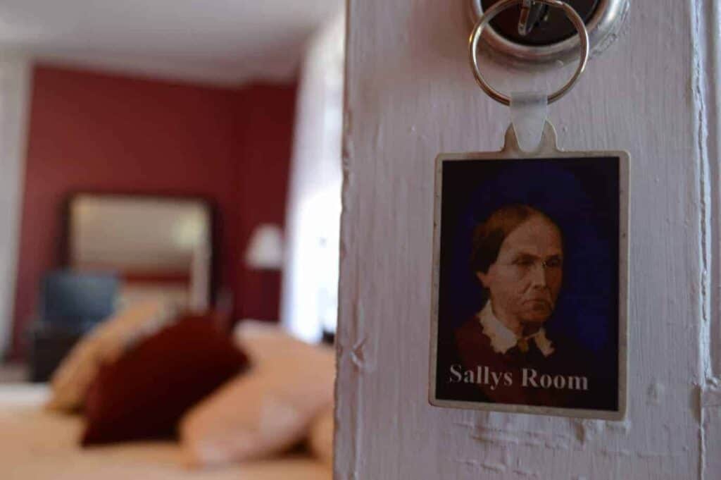 Close up of a room key, featuring a painting of a woman that says \"Sallys Room.\"