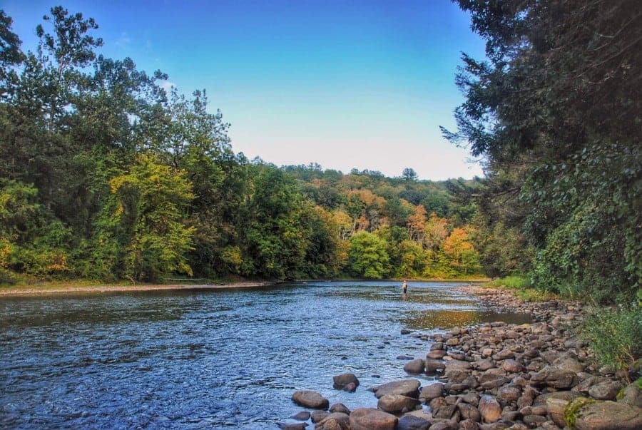 Serene river with lots of rocks. A forest surrounds the river, with pops of fall foliage in Litchfield Hills, Connecticut.