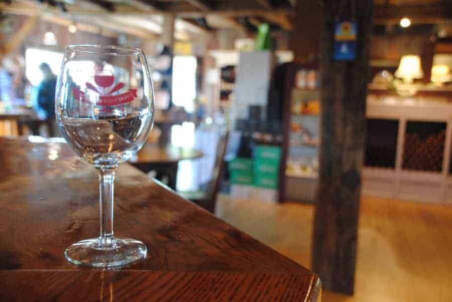 Wine glass sitting on top of a wooden counter. The inside of a restaurant is blurred in the background.