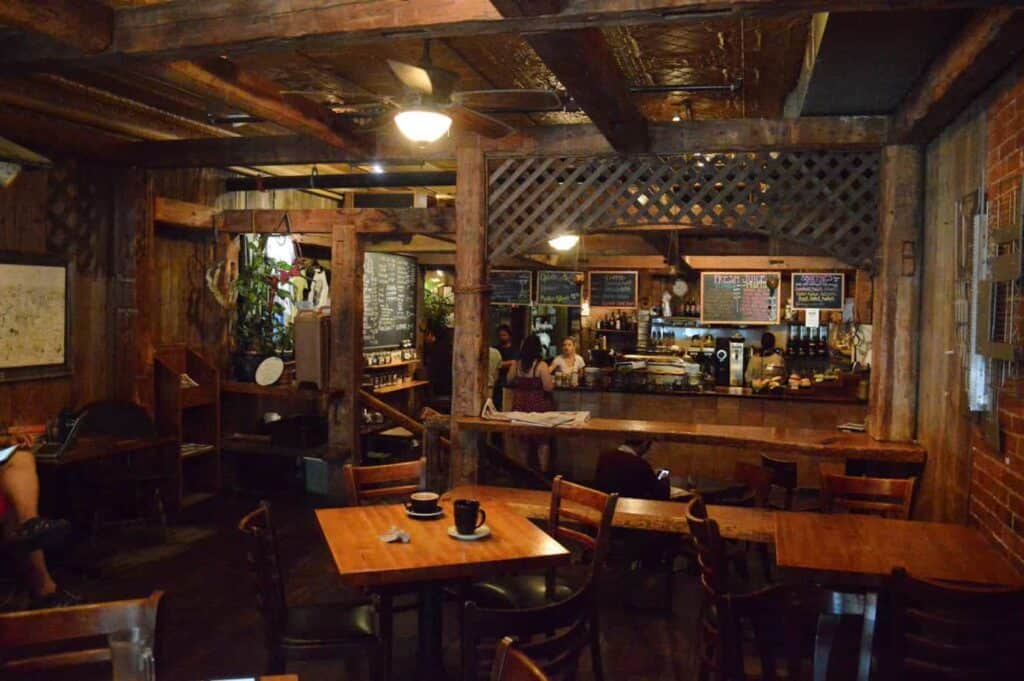 Interior of a dark Burlington, Vermont coffee shop with dark wooden walls and ceilings. In the forefront, a warm wood table is surrounded by chairs where two coffees sit.