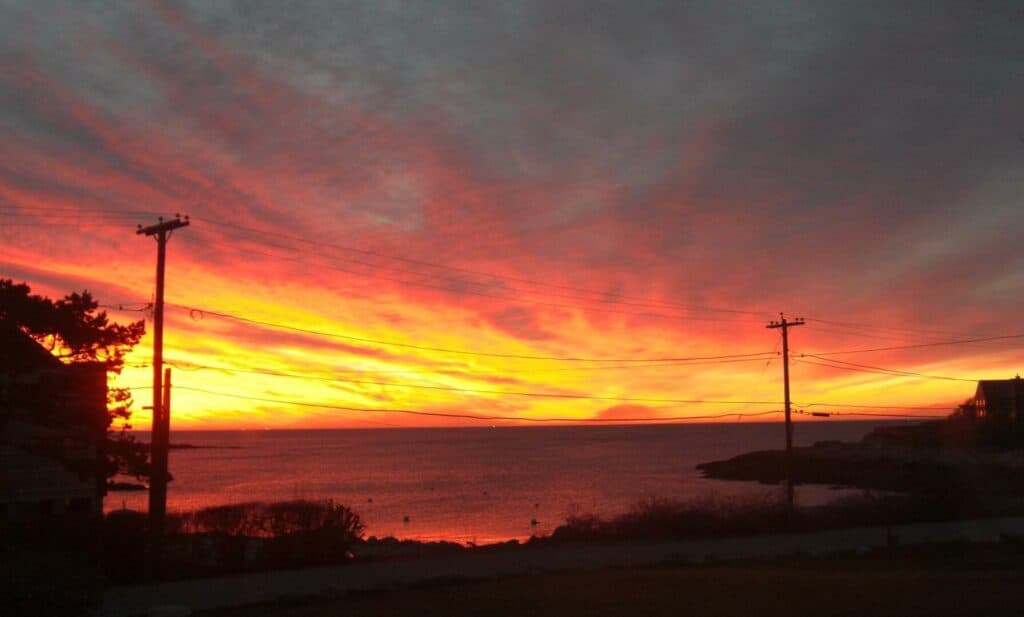 An orange and red sky reflects off the ocean at dusk.