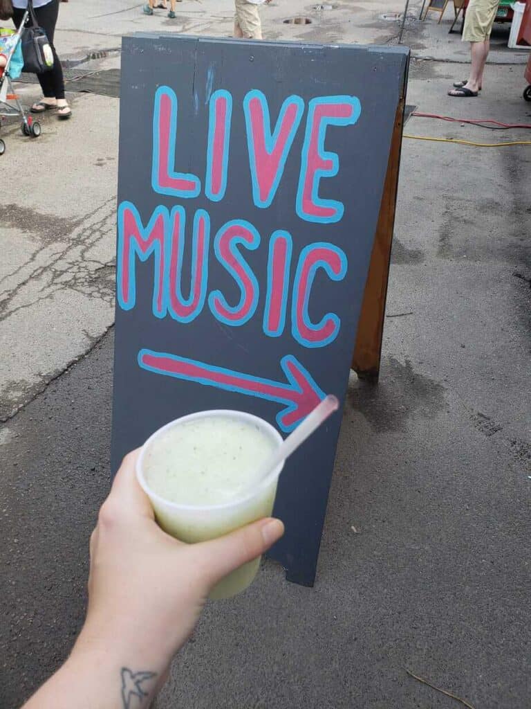 A placard reading \"Live Music\" in Burlington Vermont while a hand holds an icy drink in front