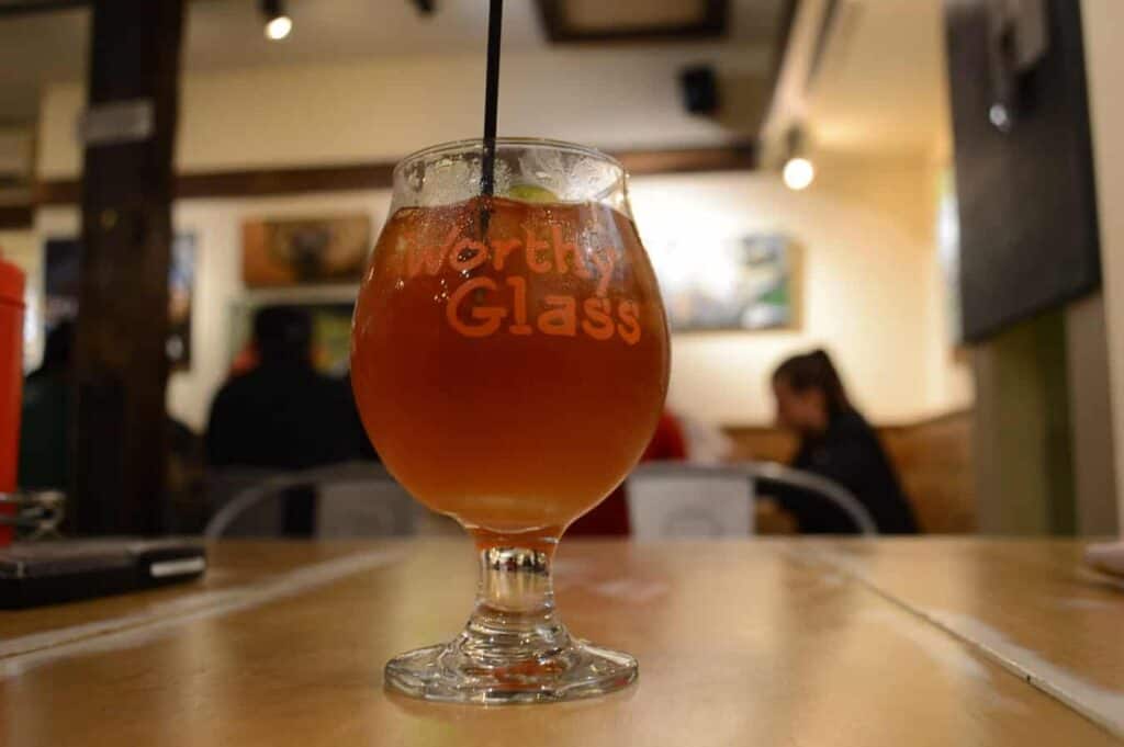 An amber liquid in a goblet that says \"Worthy Glass\" in Woodstock Vermont