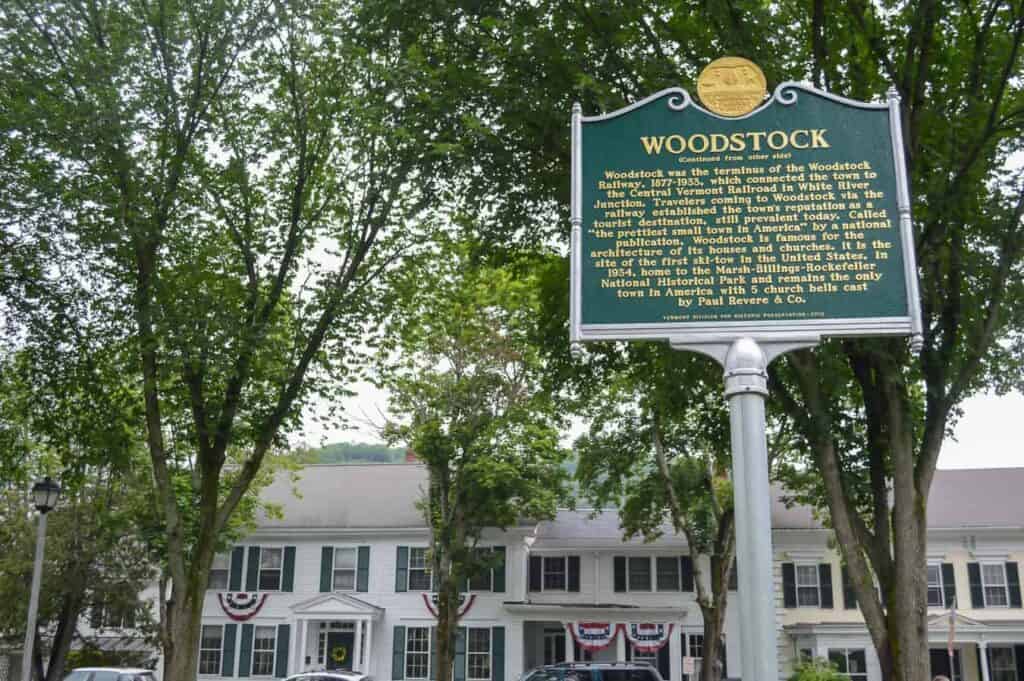 A sign talking about Woodstock in front of a large white building surrounded by green trees