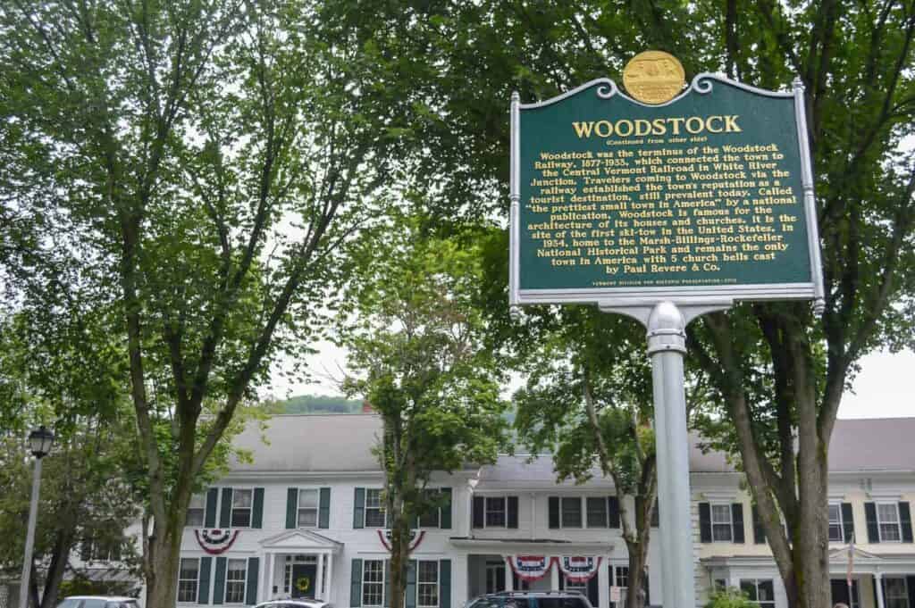 A sign in front of a large white building surrounded by green trees in Woodstock Vermont