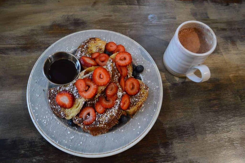 French toast with strawberries and syrup on a white plate 