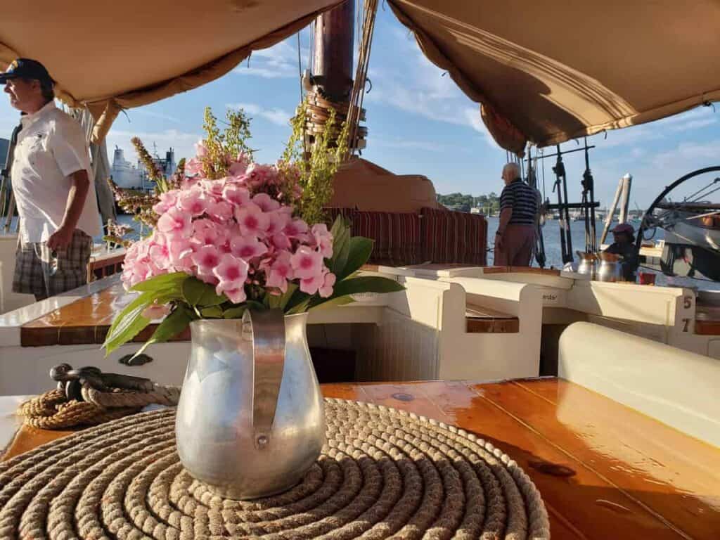 A vase of flowers on a table in the foreground. The distance shows a person peering out to the water.