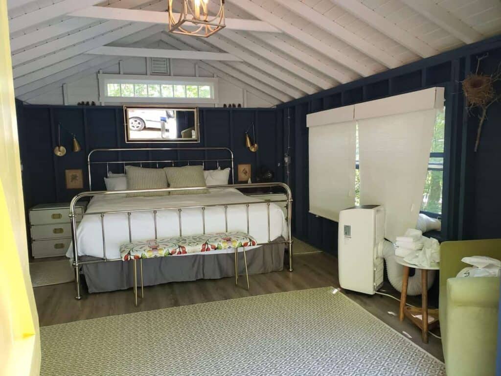 Interior of a cabin-like home. A bed is properly made with side tables and a window is above the bed.