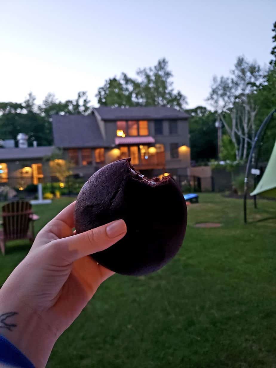 Person holding a chocolate whoopee pie with a bite taken out of it.
