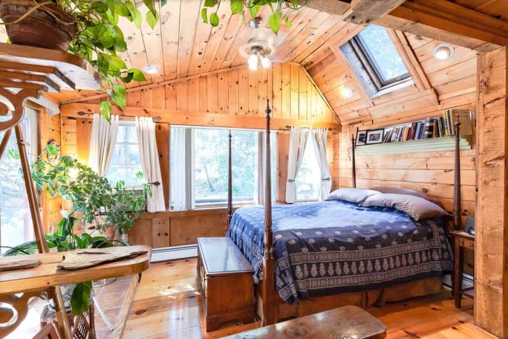 A four poster bed with a blue quilt in a wood paneled room with many windows