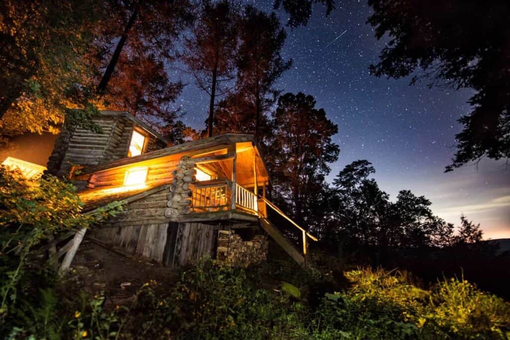 A wood airbnb cabin in Vermont up high on a hill with lights on at dusk 
