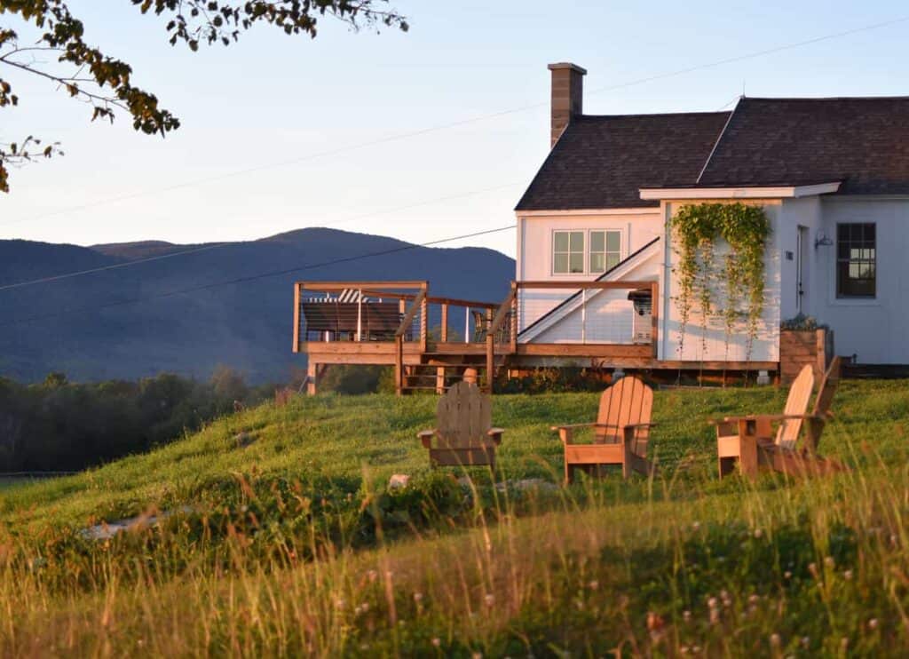 A pink house with a side deck on a hill with Adirondack chairs on the lawn at a vacation rental in New England