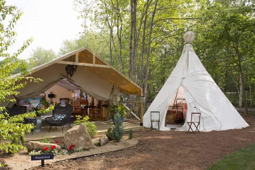 A cream teepee next to a forest. To the left is a glamping spot with tan canvas.