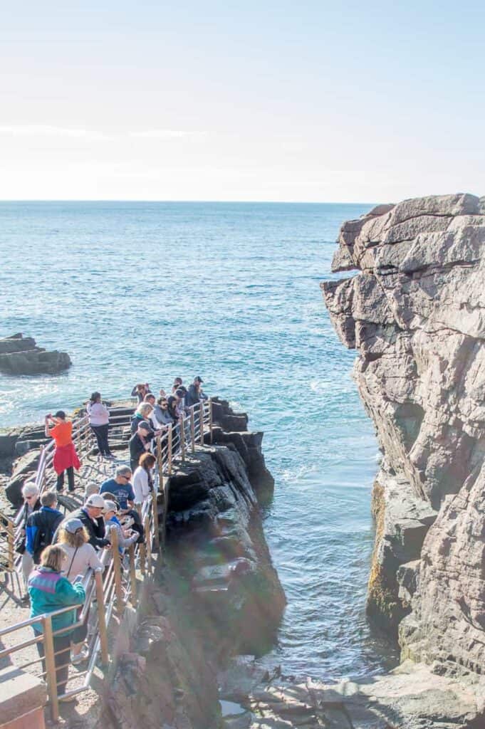 A group of people on a rock looking out at the view next to a body of water.