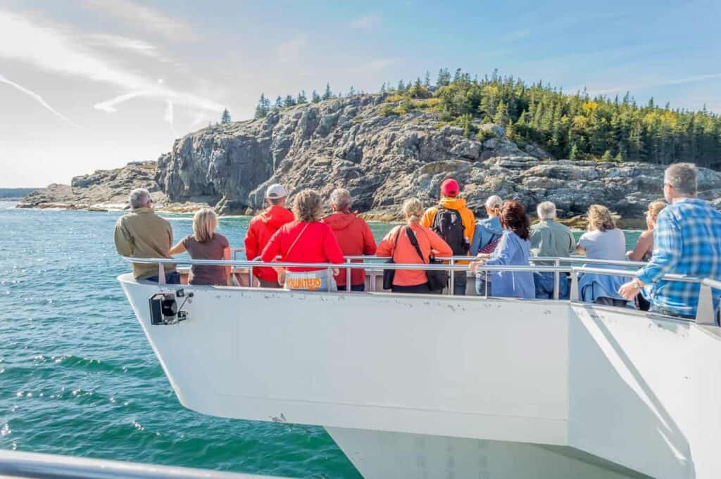 A group of people on a boat in the water looking out at the scenic cliff side on Mount Desert Island