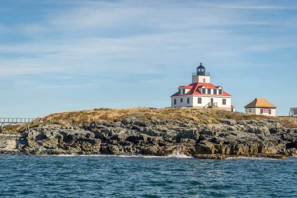 White building with a red roof on a rocky island by the water.