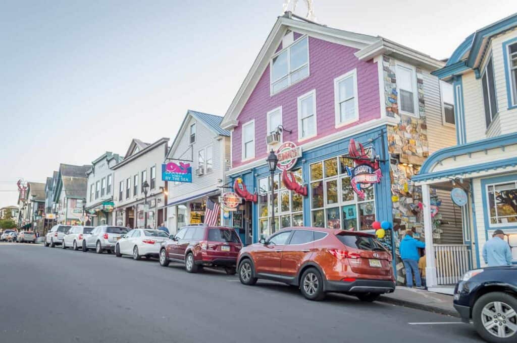 Colorful downtown shops and restaurants line a road where cars are parked under a blue sky.