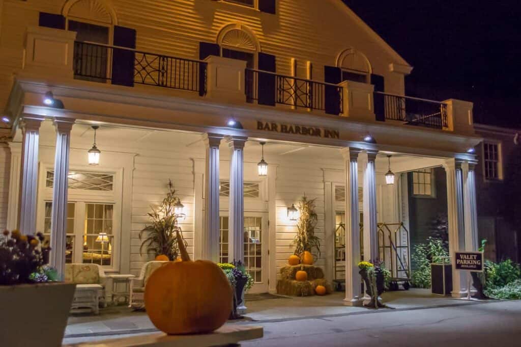 Front of a white building that says Bar Harbor Inn at night. A pumpkin is perched in the foreground near Acadia National Park.