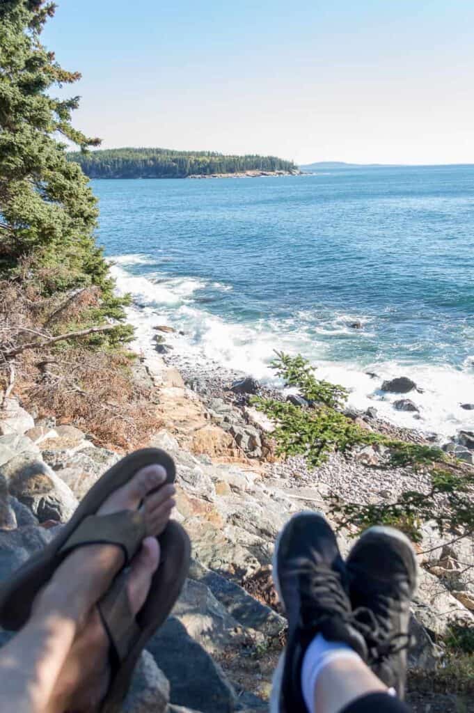 Feet of two people in the foreground who are looking out at the blue beach.