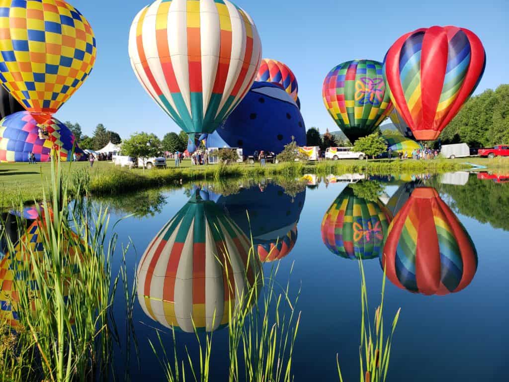 Colorful hot air balloons are reflected in a nearby pond. this is the stowe balloon festival one of the best things to do in Stowe Vermont