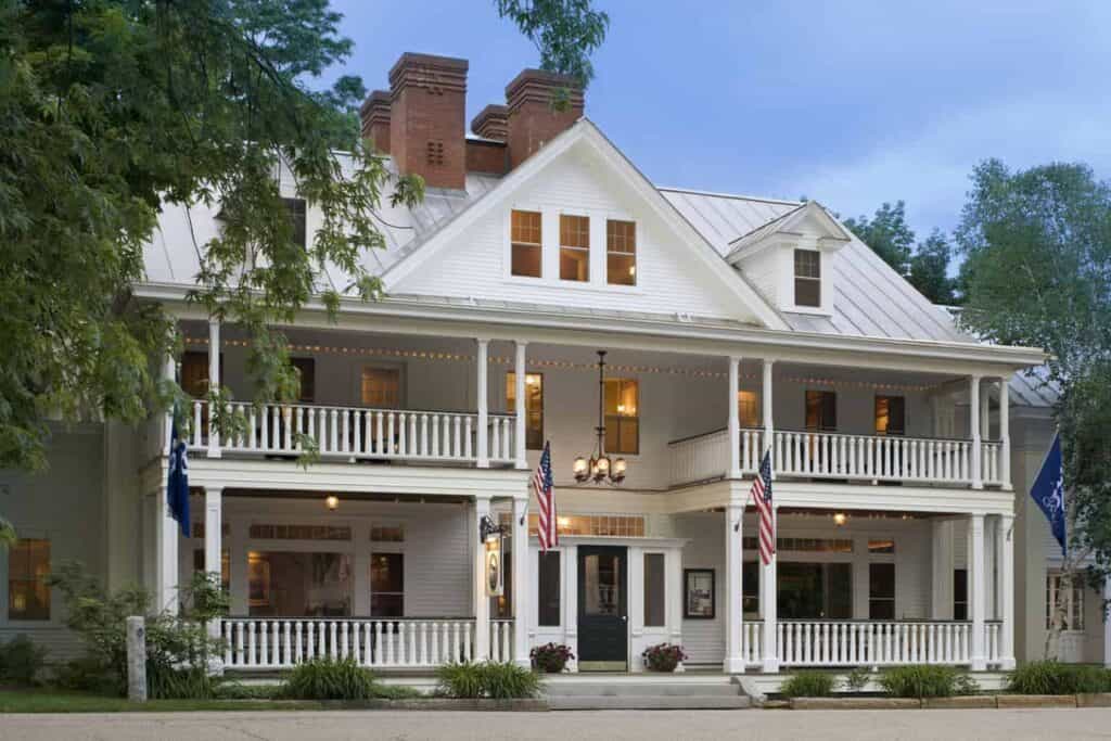 New England style white inn with two American flags hanging from the entrance under a blue sky.