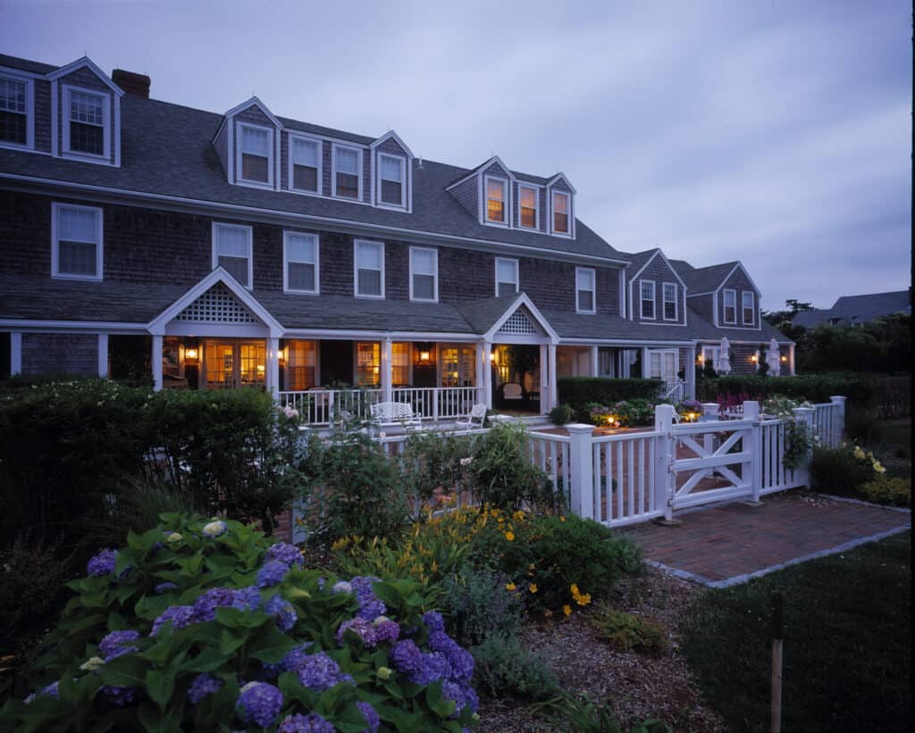 Large historic hotel is lit up by orange lights in the evening under a grey sky.