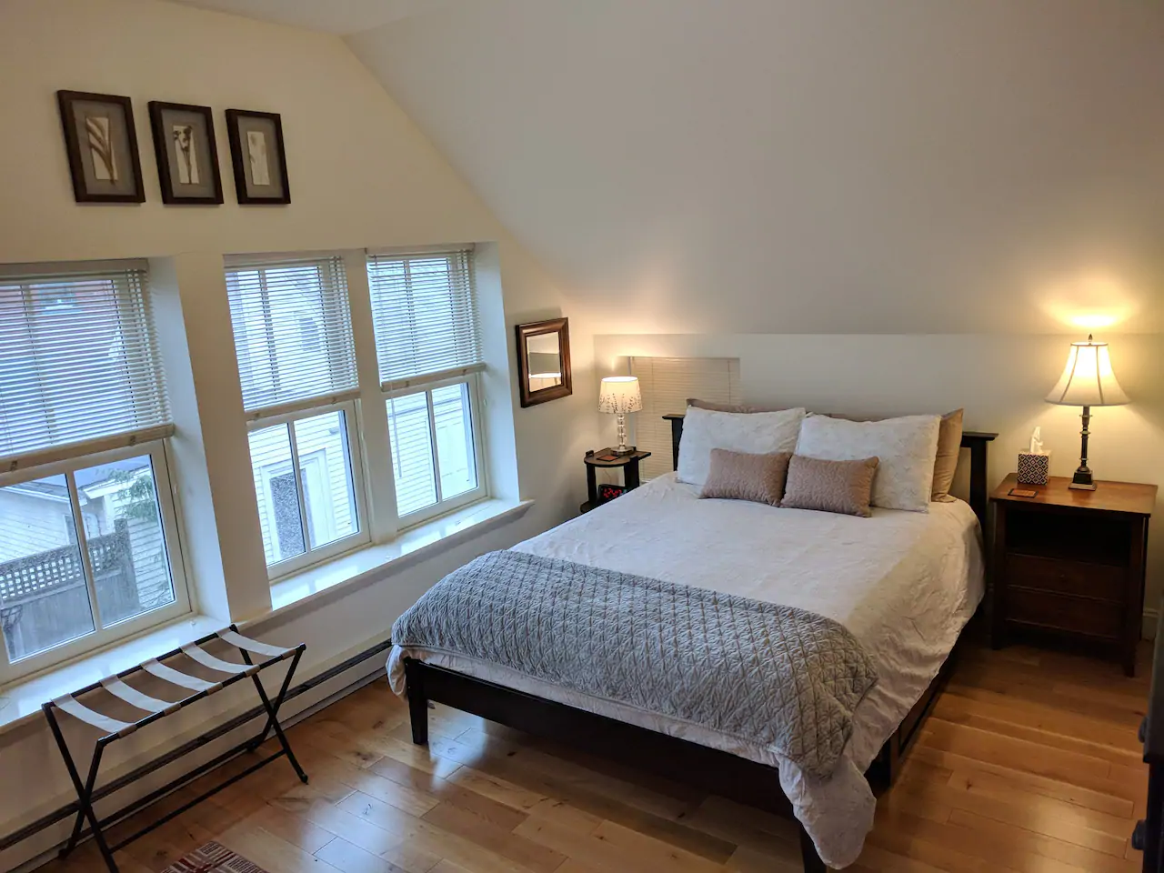 White bed perfectly made next to a set of windows in an arch-roofed room.