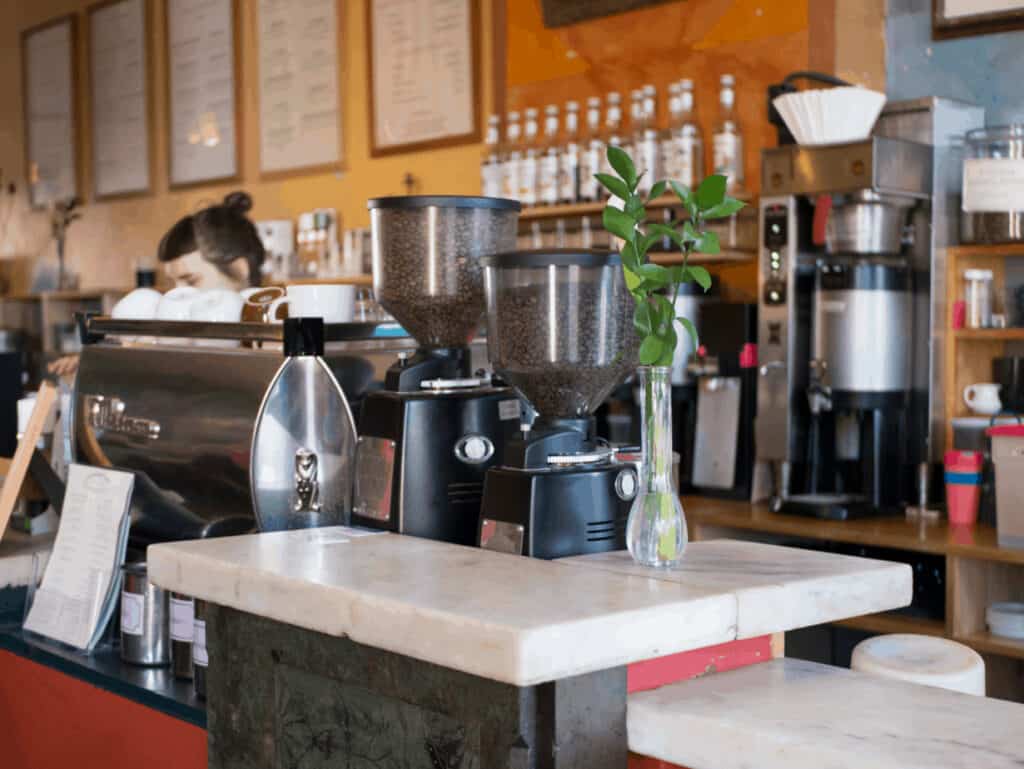 Close up of an espresso machine with beans in it. A barista can be seen behind, making coffee in Northampton MA.