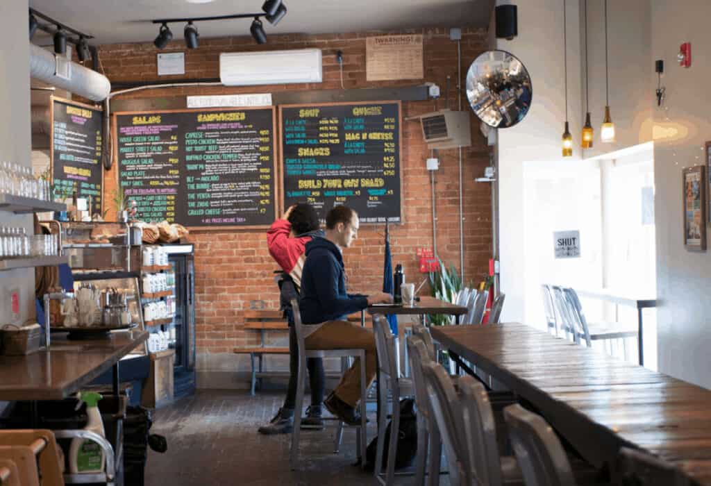 People working at a wooden table in a cafe. A brick wall is behind them at a Northampton coffee shop.