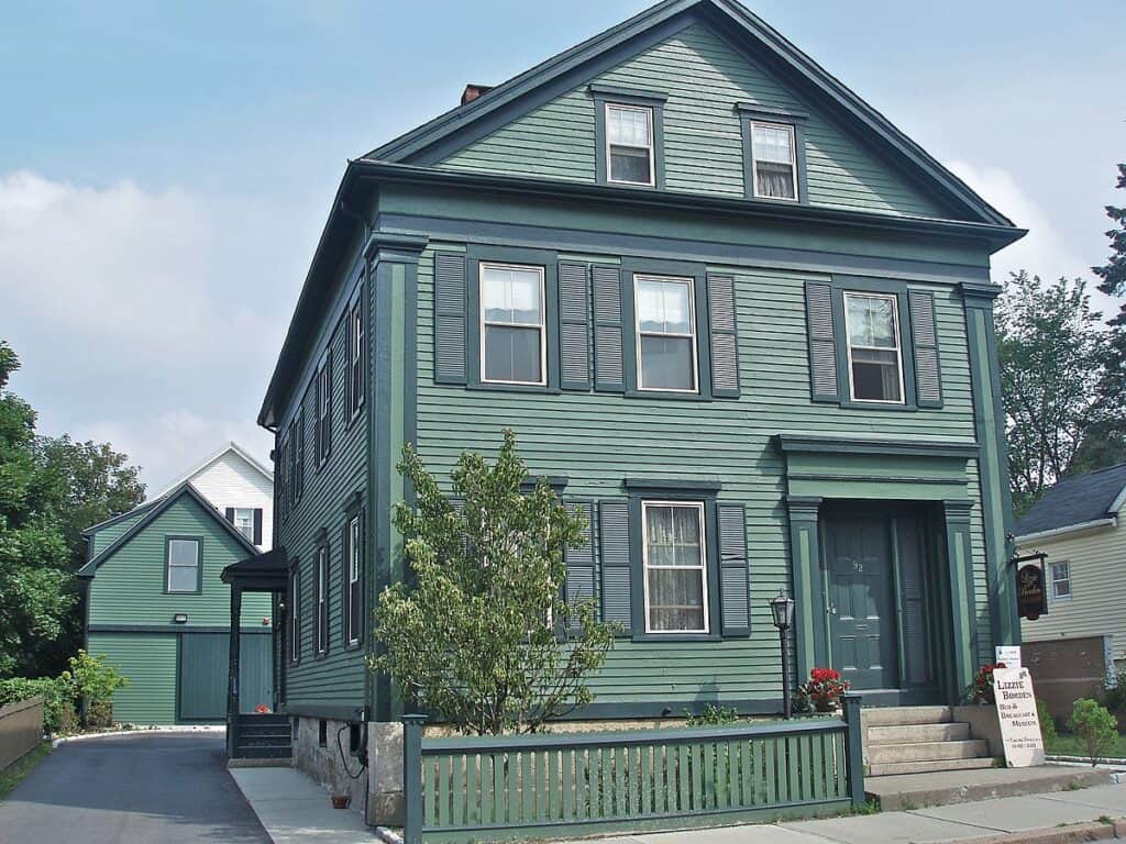 Light blue clapboard house in New England with steps going up to the front door, a short wooden fence across the front of the house 