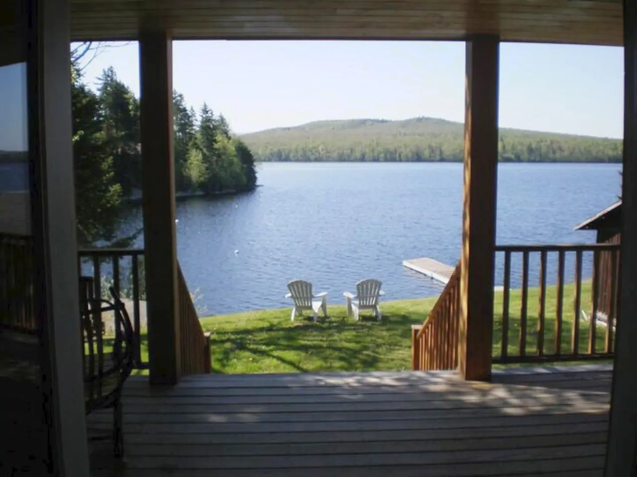 Wooden deck overlooking 2 chairs at the edge of the lawn overlooking a lake with mountains in the distance