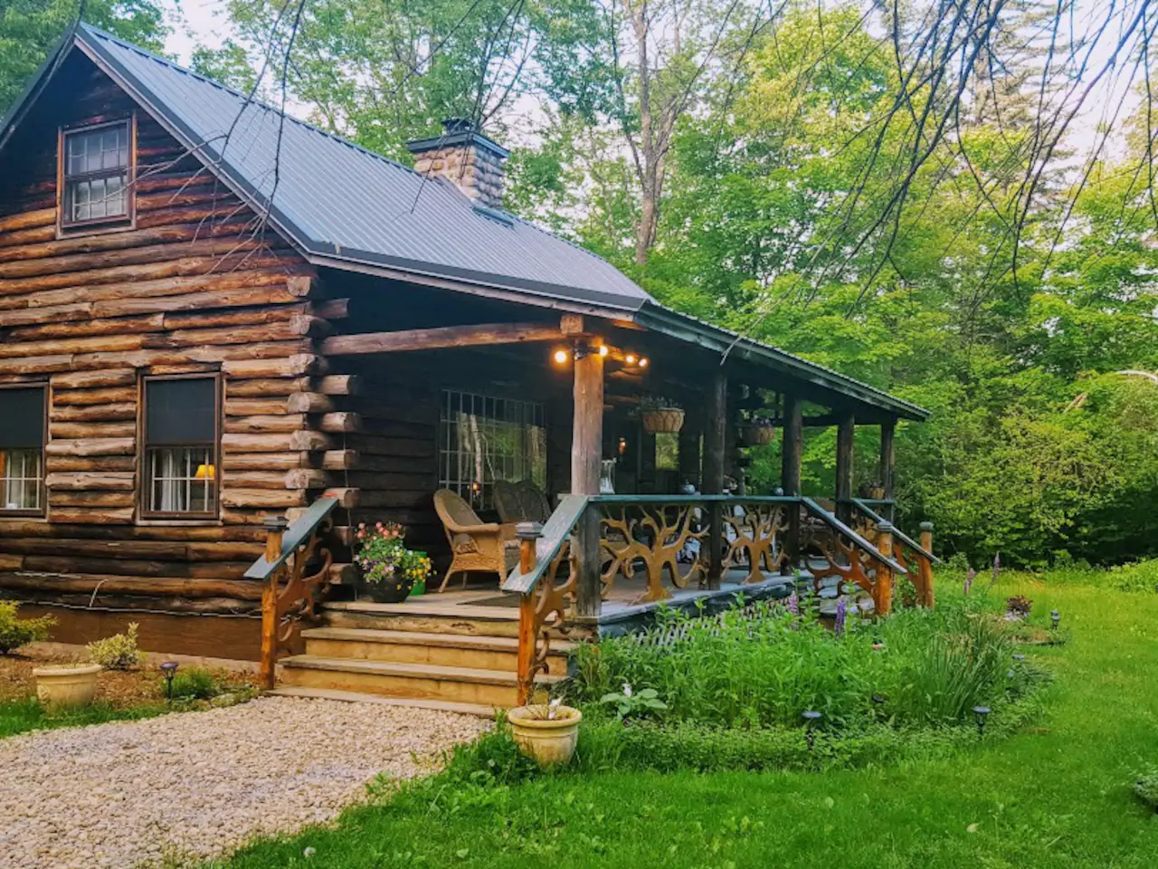 Log cabin in the woods with steps leading up to a porch with chairs