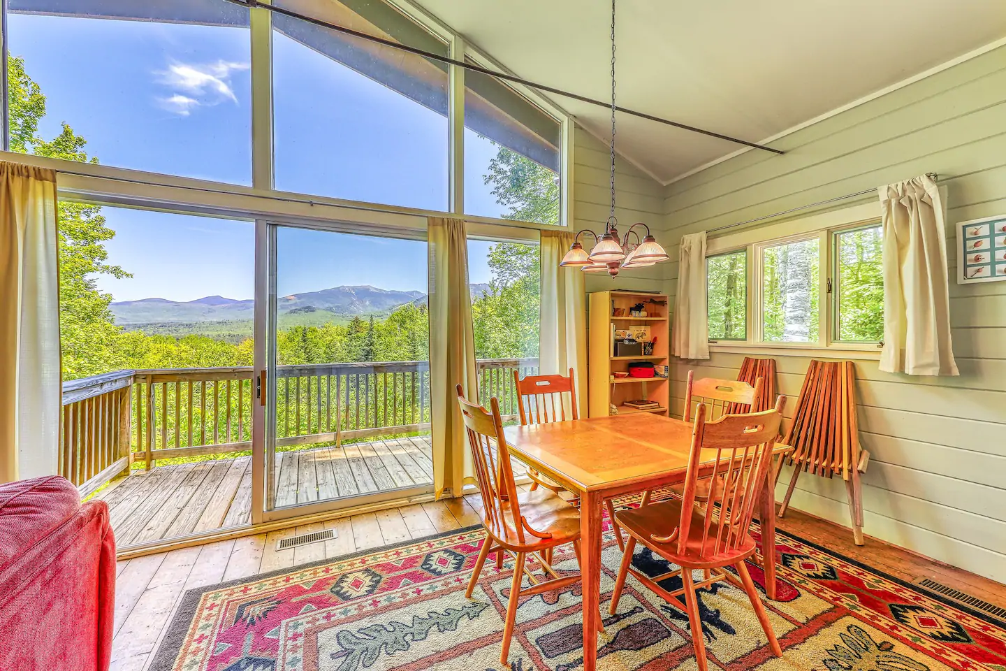 Bright kitchen with table and chairs with a wall of windows overlooking a wooden deck and mountains in the distance